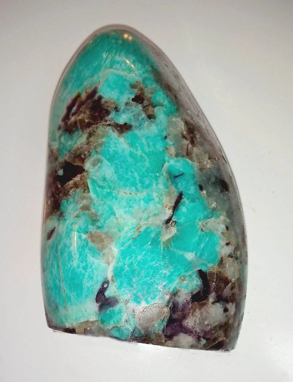 Polished amazonite specimen with blue-green and dark matrix areas.