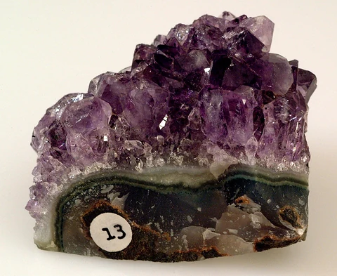 Cluster of violet amethyst crystals on the banded base of a geode.
