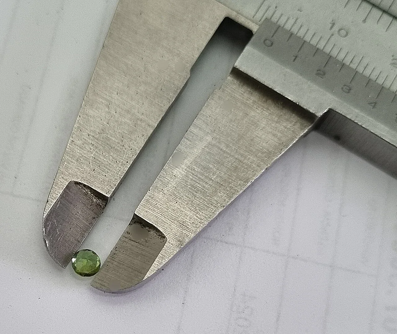 Small green faceted tourmaline beside a caliper