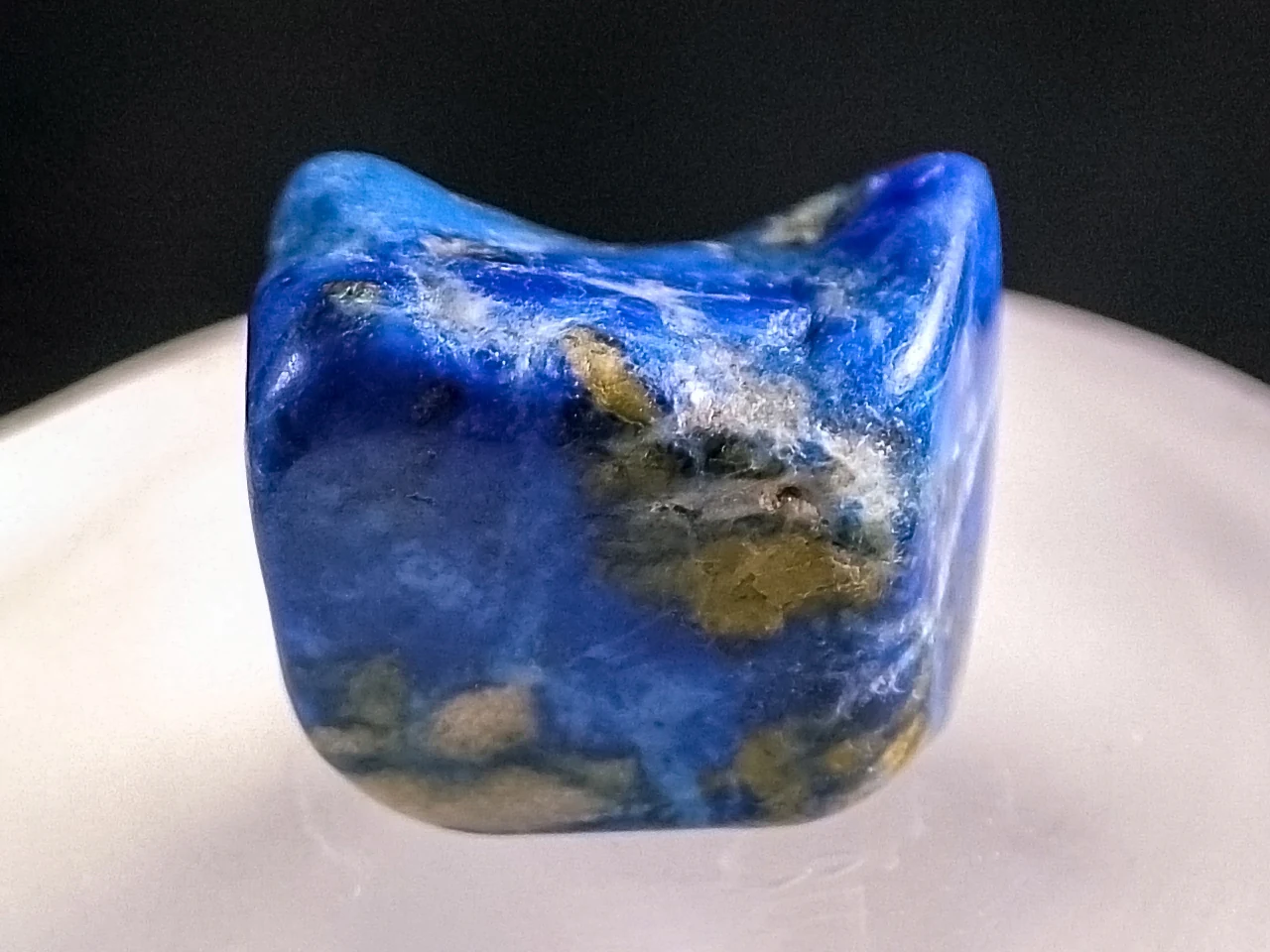 Polished lapis lazuli pebble with blue, pale and gold-coloured areas.