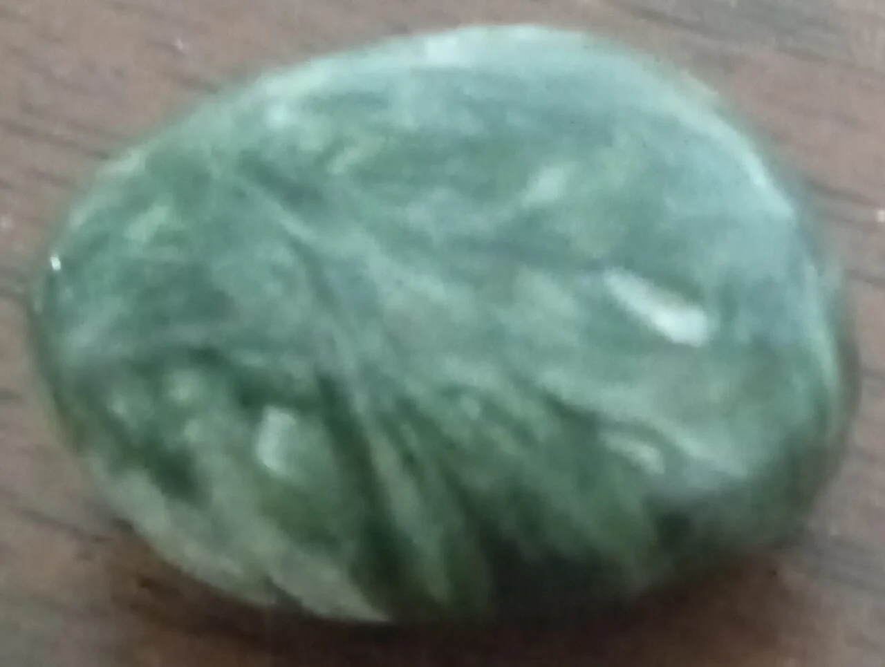 Green polished seraphinite on a wooden background