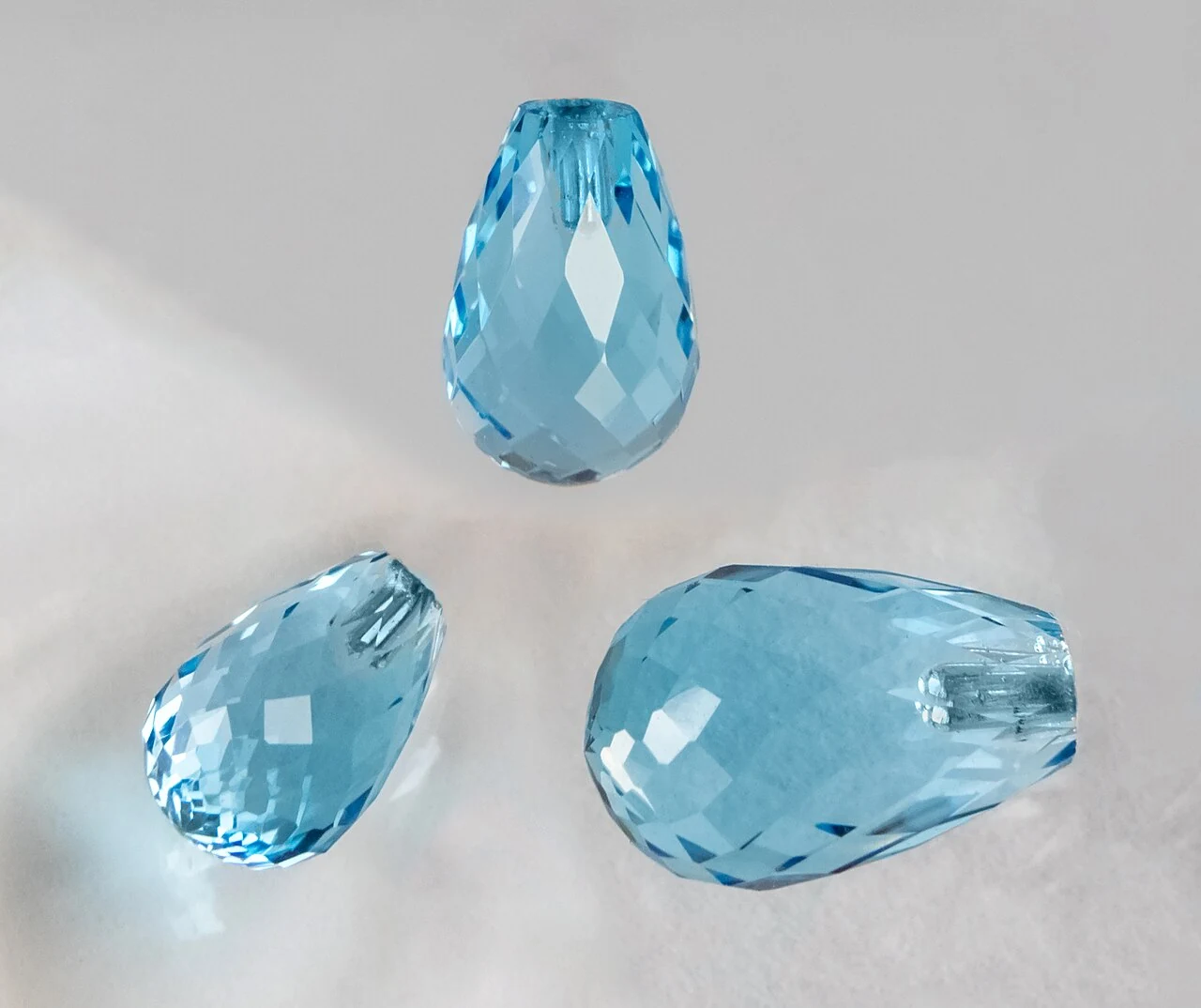 Three views of a blue faceted topaz briolette